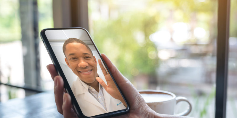 Woman's Hands Holding Black Mobile Phone With Doctor On Screen