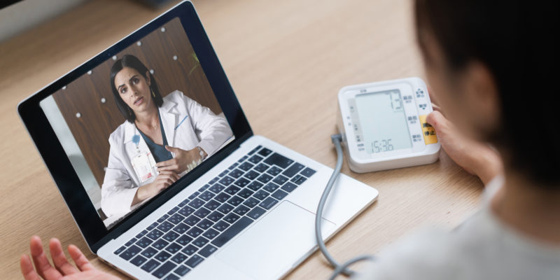 A Woman Is Measuring Her Blood Pressure While Consulting With A Doctor Via Telemedicine Video Call On A Laptop At Home