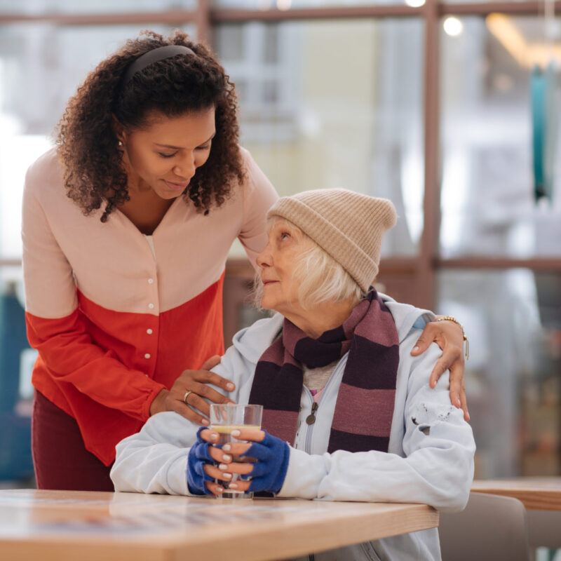 Being thirsty. Pleasant unhoused woman sitting at the table while wanting to drink water