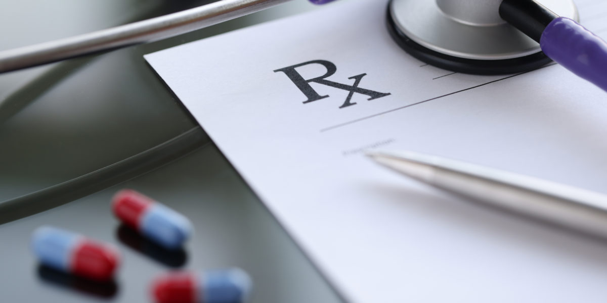 Ballpoint pen lying on medical prescription near phonendoscope in doctors office. Illegal prescription of drugs concept